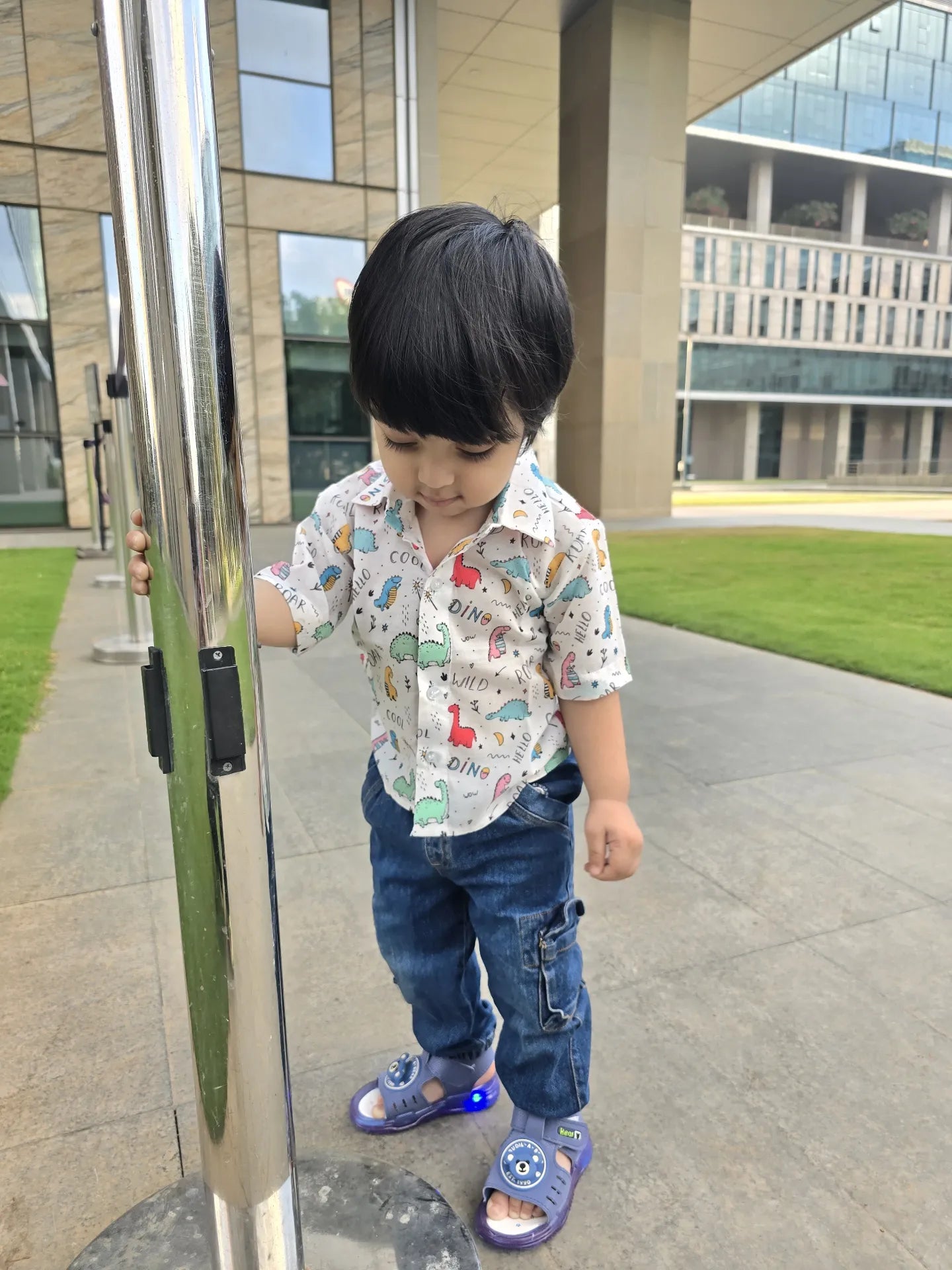 Child wearing a patterned shirt and blue jeans standing near a building entrance.